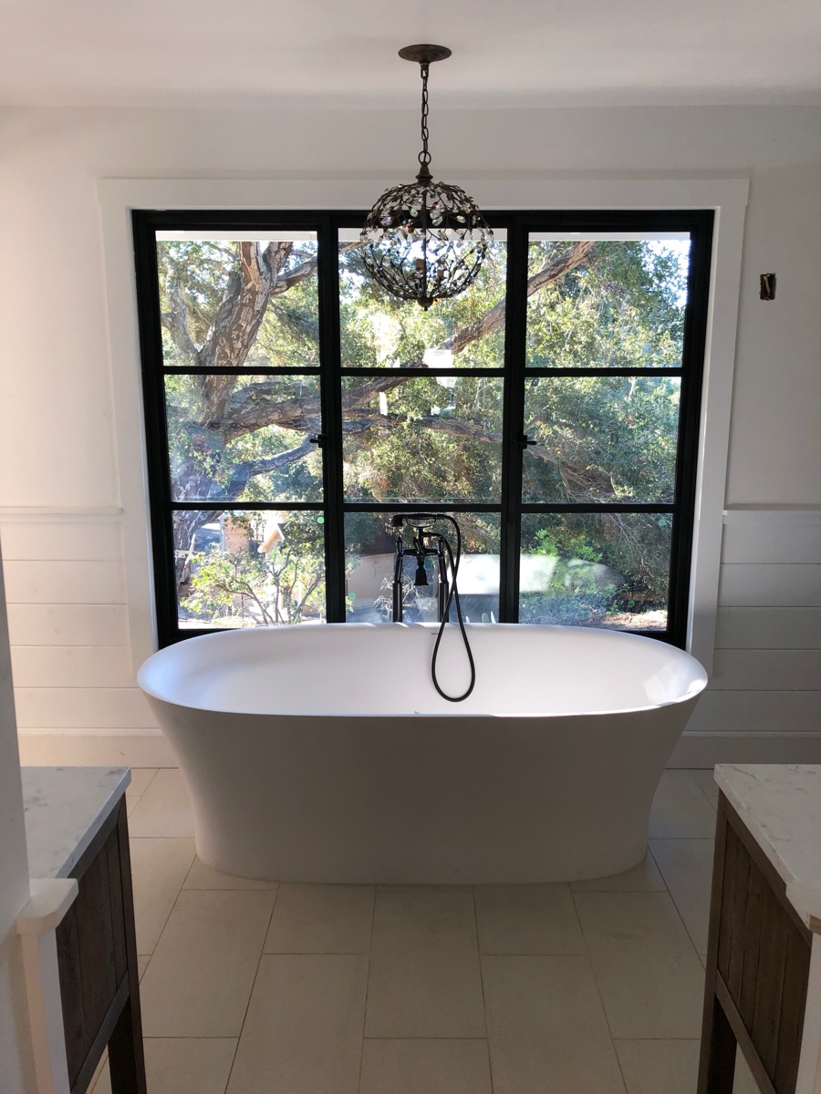 Freestanding soaking tub with black steel-frame window and chandelier